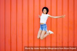 Woman in shorts and t-shirt jumping with knees bent against red wall 56r7d5