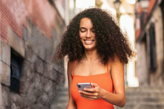 young woman with curly hair walking and using her mobile going down stairs