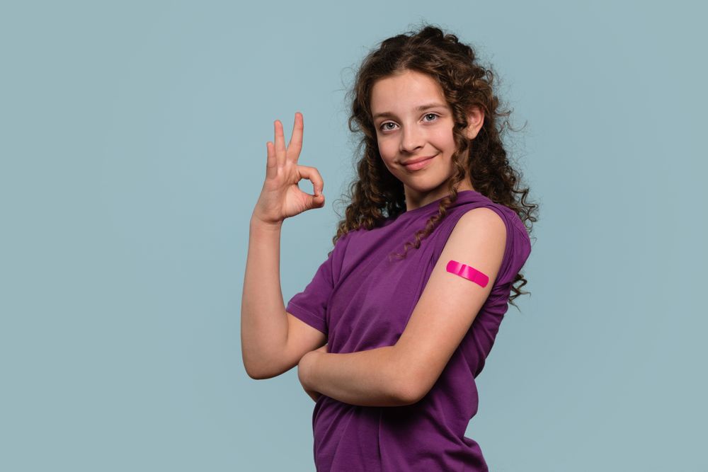 Girl making "OK" gesture with pink bandage on vaccinated arm