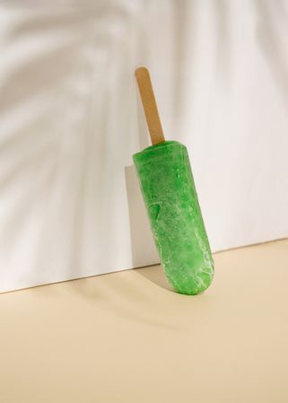 Lime ice pop leaning on beige wall with palm tree shadow