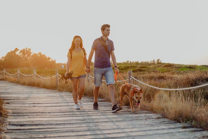 Casual adult couple walking with dog along rural pathway
