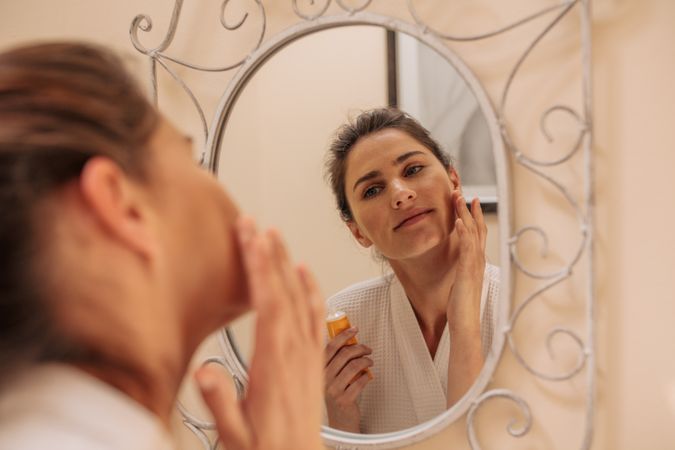 Female in mirror applying cream on her face