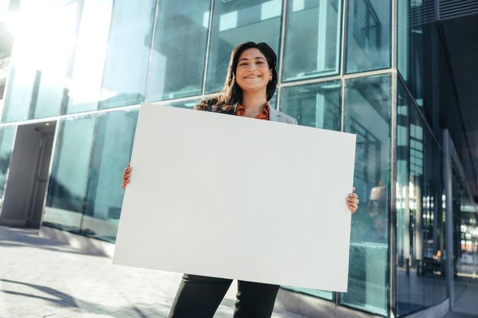 Businesswoman holding a blank poster while standing in front of a high rise urban building
