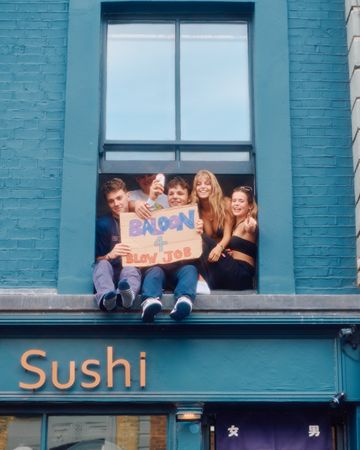 London, England, United Kingdom - August 27, 2022: Friends with funny sign hanging out window