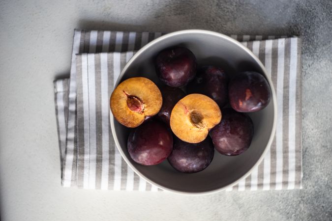 Top view of bowl of halved ripe plums with copy space