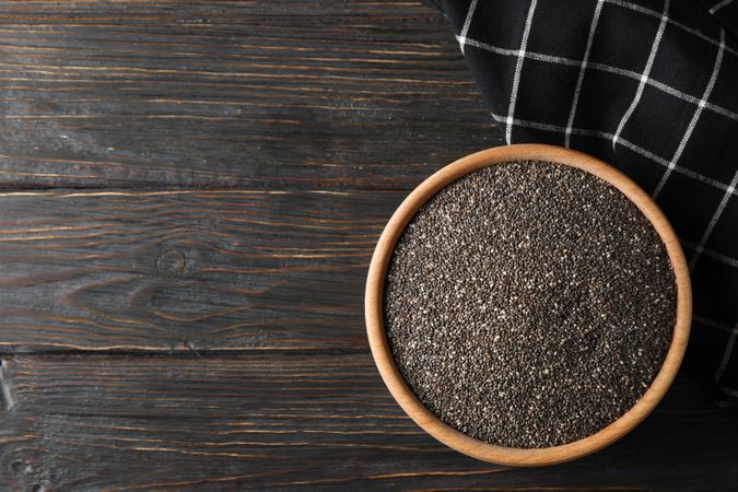 Chia in wooden bowl on wood background, top view