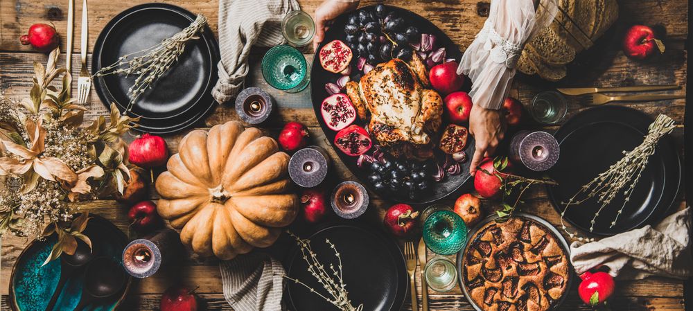 Thanksgiving table setting for gathering with woman serving roast chicken plate, wide composition