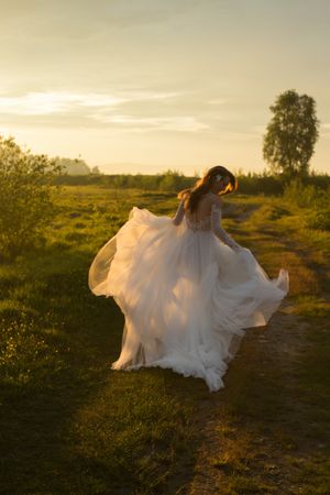Back view of bride walking on green grass field at sunset