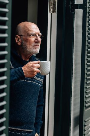 Man with gray hair standing near the door drinking coffee