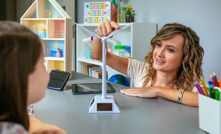 Teacher showing windmill to schoolgirl in ecology classroom