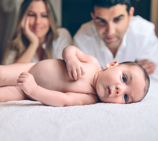 Newborn lying over bed and couple smiling on background