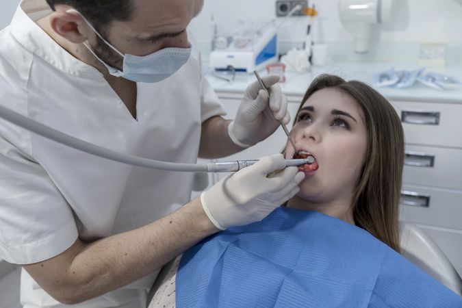 Dentist examining female teenager's teeth in clinic