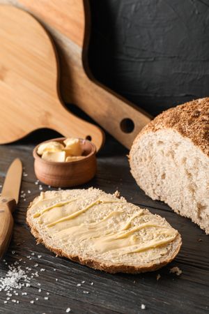 Cutting boards, bread, salt, knife and butter on wooden table against dark background, space for text