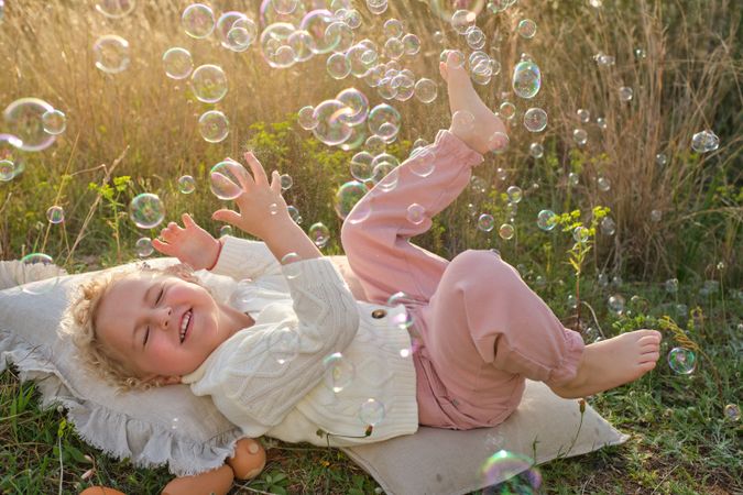 Joyful girl lying on glade and playing with soap bubbles