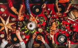 Group of people with drinks at festive red table setting with cake, roast chicken, decorations