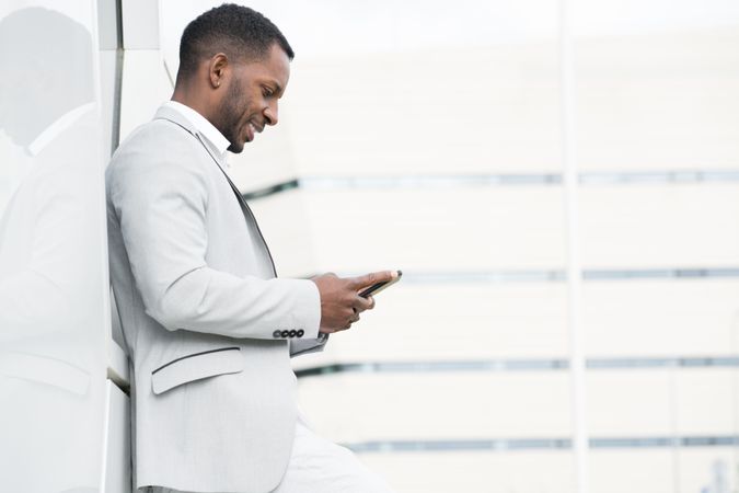 Elegant Black man browsing smartphone leaning on geometrical wall