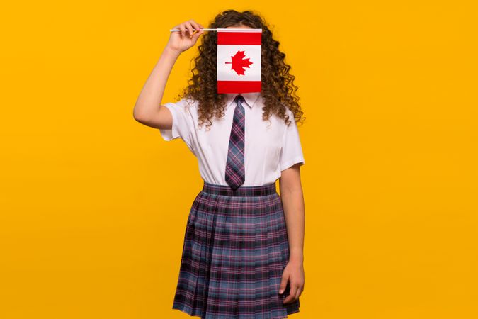 Girl in uniform hiding face behind Canadian flag