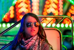 Smiling young woman near illuminated ferris wheel at night
