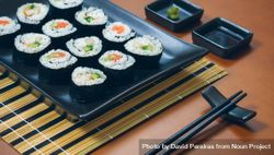 Fresh sushi rolls plated on rectangular tray on mat with chopsticks 4B1eB5