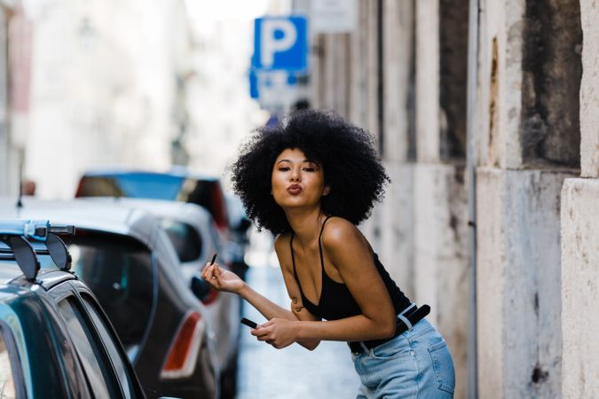 Black female applying lipstick outdoors