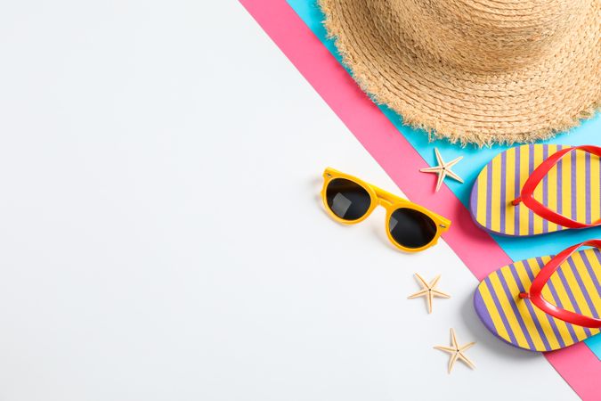 Flip flops, sunglasses, starfishes and straw hat on color background