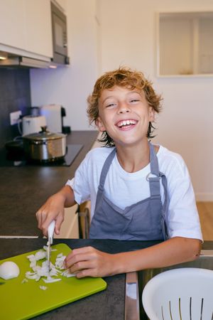 Happy boy cutting fresh onion while cooking in kitchen
