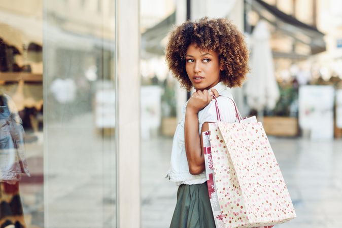 Woman standing on street with shopping bags in front of window looking over her shoulder