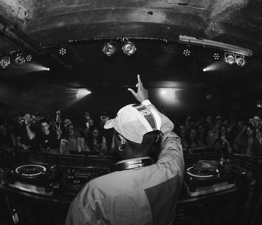 Fisheye shot from behind young DJ on stage holding hand up to audience