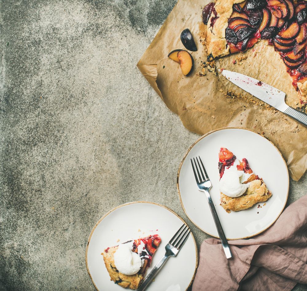Two plates of fruit tart with whipped cream, with parchment paper, knife, square crop and copy space