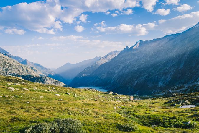 Green lawn at foot of rocky mountains under bright sky