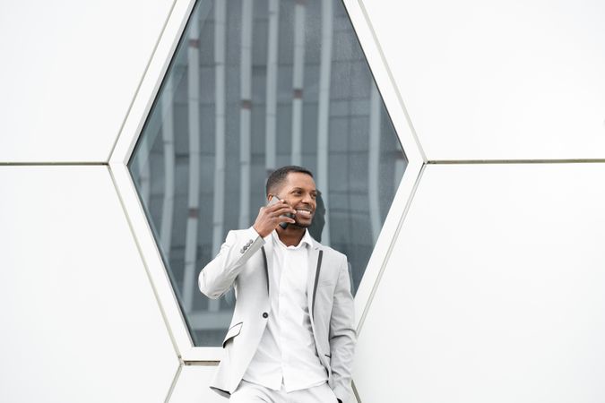 Elegant Black man talking smartphone leaning on geometrical wall