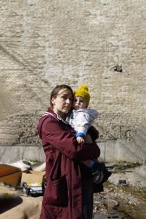 Woman holding her baby looking at rubble in front of brick wall