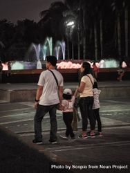 Back view of a family walking near water fountain at night 5lw2v0
