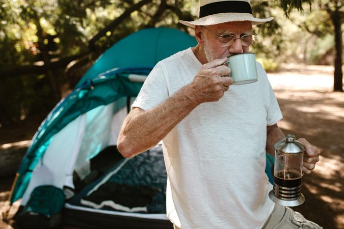 Older man having coffee at campsite.
