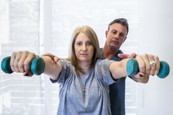 Male physiotherapist teaching a patient how to use dumbells for wellness and disability support.