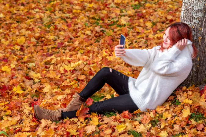 Woman leaning on tree trunk taking selfie in autumn