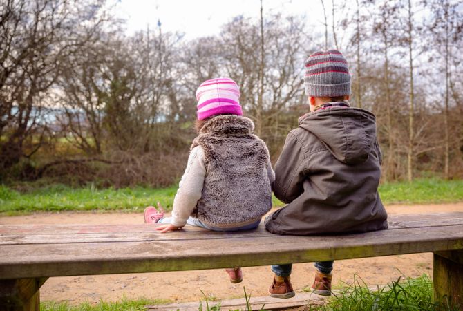 Back of little boy and girl sitting on park bench in forest