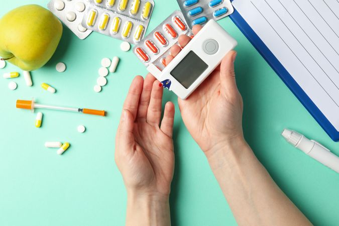 Female checking blood sugar level on background with diabetic accessories