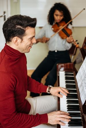Man playing piano near woman playing violin in studio