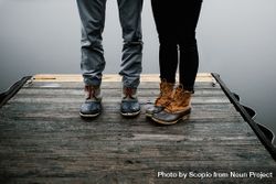 Two people standing on wooden dock beside body of water 43VZZ5