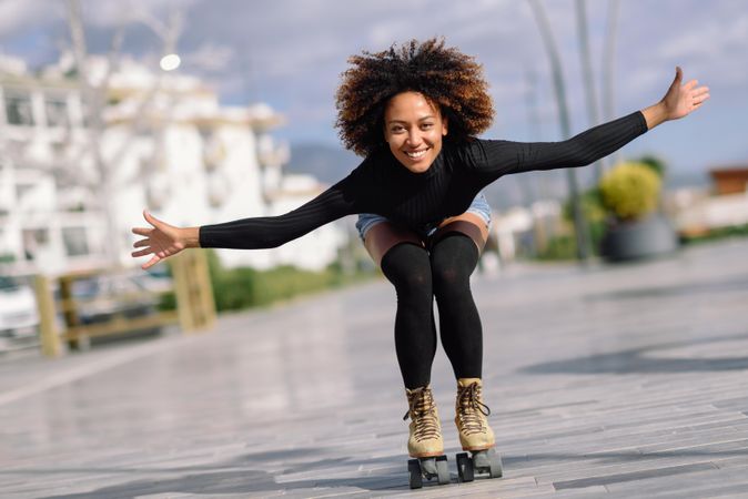 Black female with afro and arms spread roller skating outside
