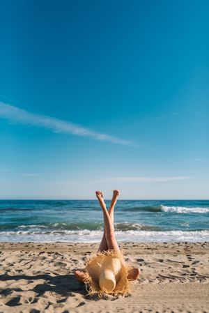 Woman in big hat lying on sandy beach