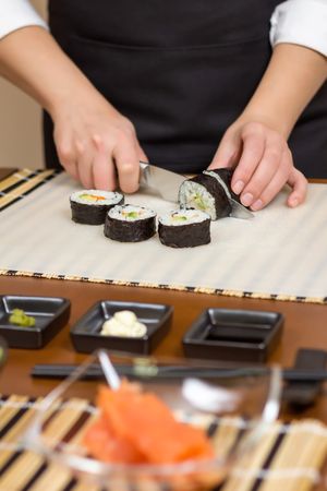Female chef cutting Japanese sushi rolls with rice, avocado and shrimps in nori, vertical