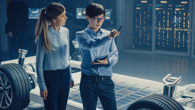 Male and Female Automobile Design Electric Car Engineers Having Conversation, Use Clipboard to Check Maintenance Issues.