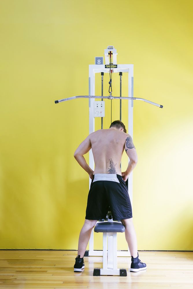 Back of tattooed male sitting down on pull down machine