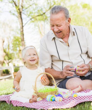 Grandfather and Granddaughter Coloring Easter Eggs on Blanket At Park