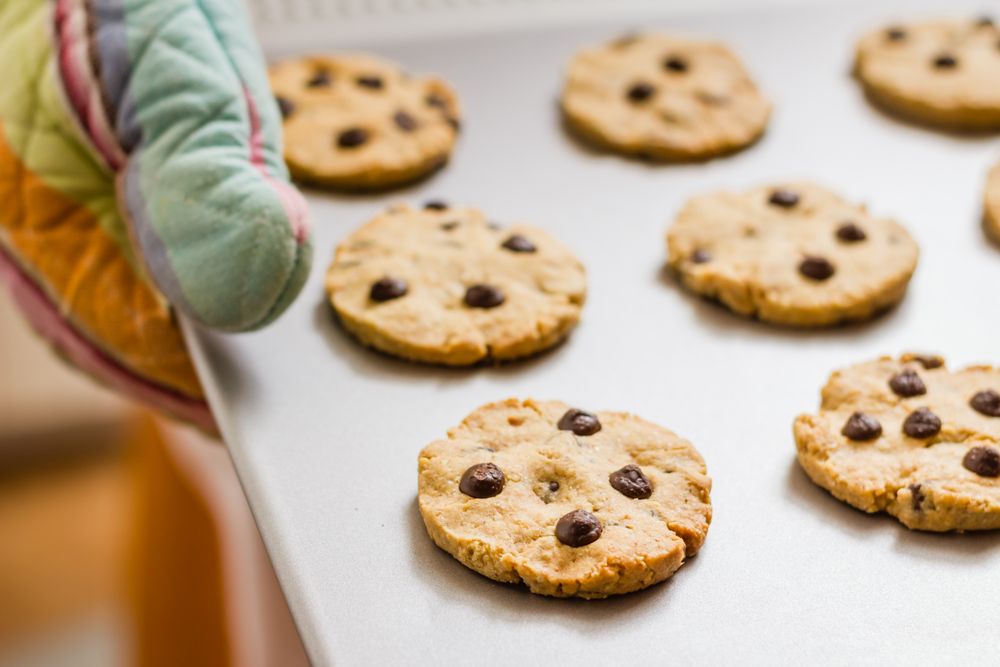 Woman holding a tray with baked cookies with kitchen gloves