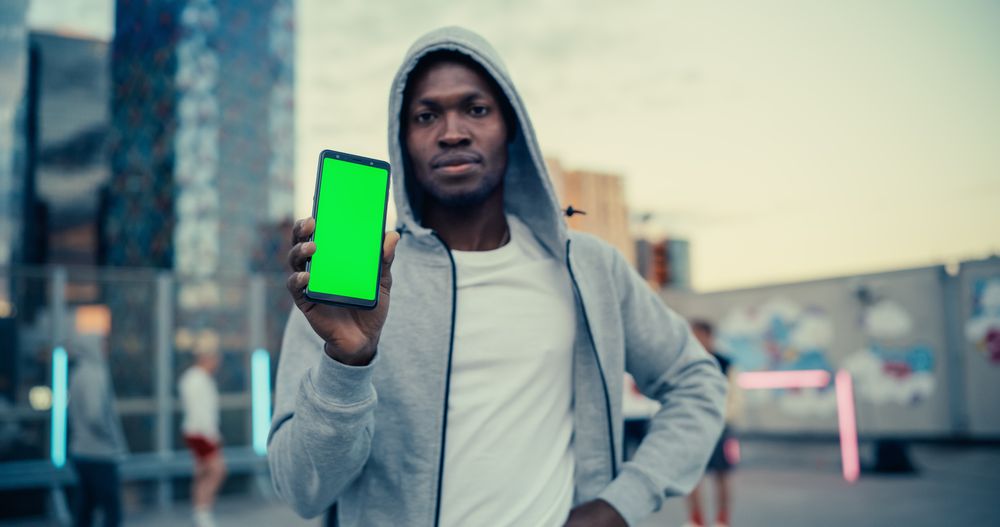 Black Man Holding a Smartphone, Showing the Green Screen Mock Up Display.