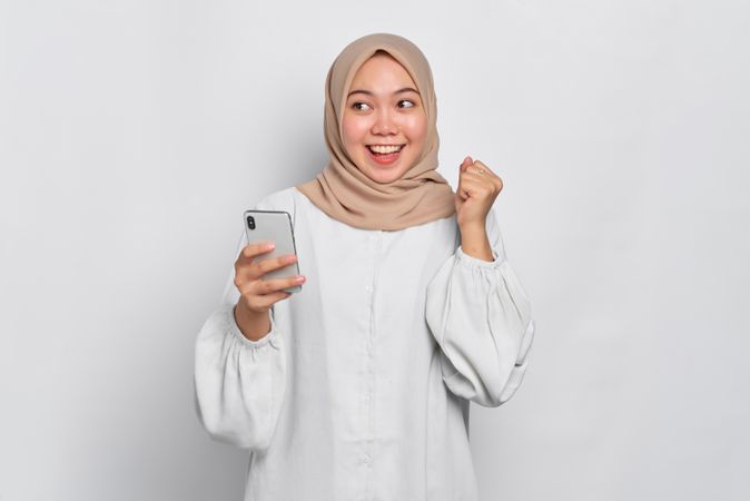 Asian female in headscarf looking happy and looking away from her cell phone