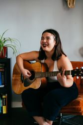 Young woman sitting in orange chair holding guitar and laughing with eyes closed